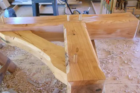 A wooden bench with two metal hooks on it.